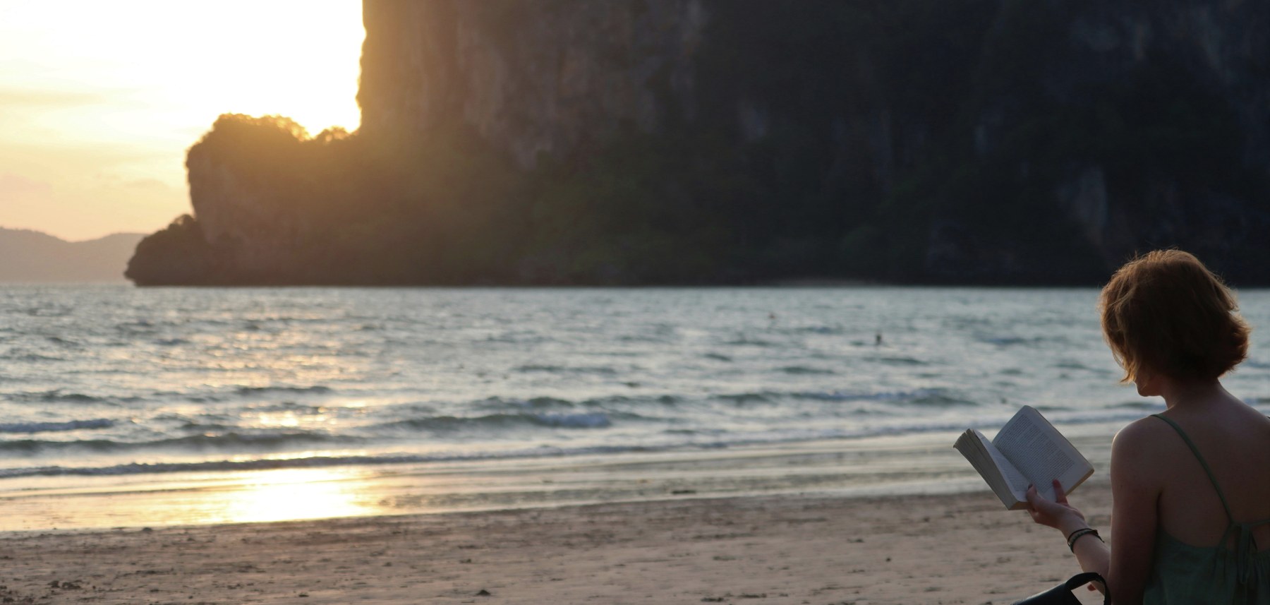 A woman reading a book on a beach at golden hour