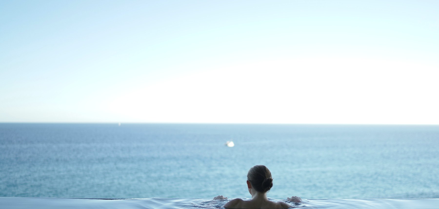 A swimmer in an infinity pool gazing out to a calm sea
